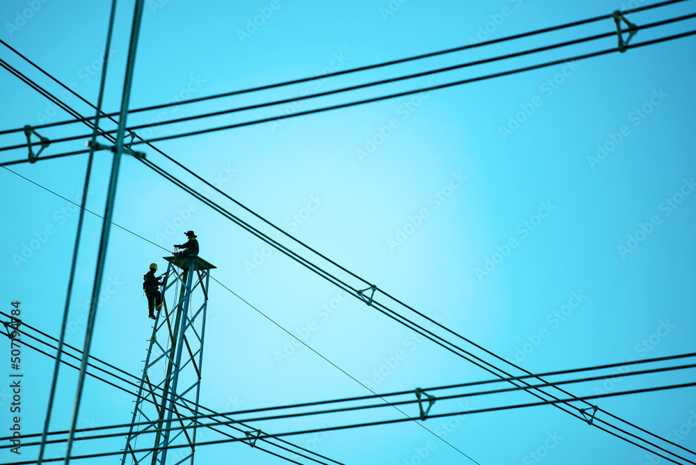 Silhouette electrician work installation of electricity lines in high voltage stations safely and systematically over blue sky background. Manual labor and industrial concept. Silhouette electrician work installation of electricity lines in high voltage stations safely and systematically over blue sky background. Manual labor and industrial concept.
