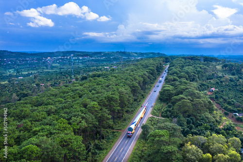 Aerial view of long vehicle truck with special semi-trailer for transporting oversized load or exceptional convoy through a rural forest and mountainous area. Transportation and logistics concept