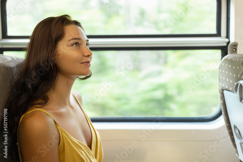 Travel and exploration of happy tourist woman by train in first class wagon to famous places of the country. Romantic smiling young traveler woman enjoying comfortable train ride, looking out to the