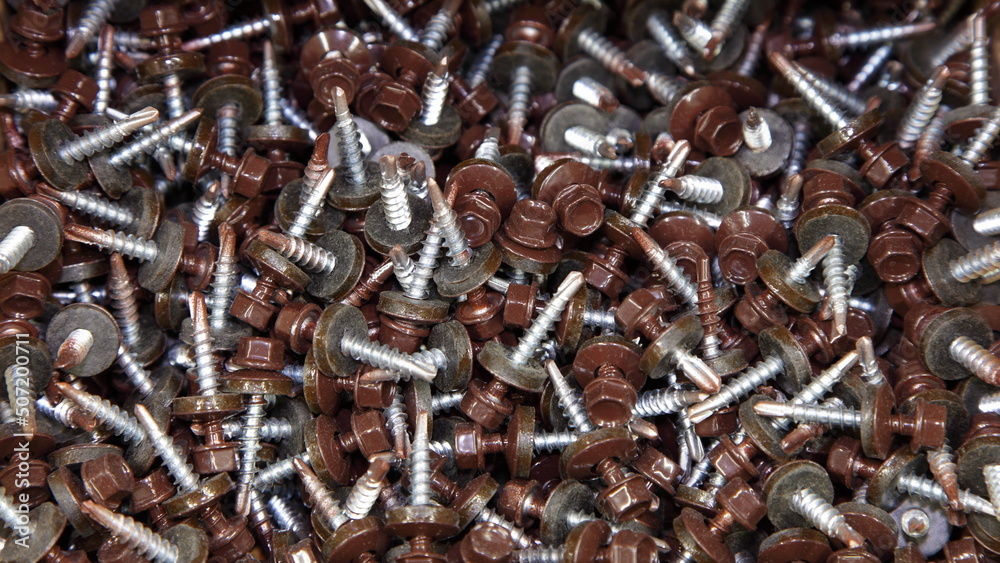 A lot of new brown RAL painted roofing self-tapping screws with washers. Galvanized construction fasteners. Technical texture for the background. A lot of new brown RAL painted roofing self-tapping screws with washers. Galvanized construction fasteners. Technical texture for the background.