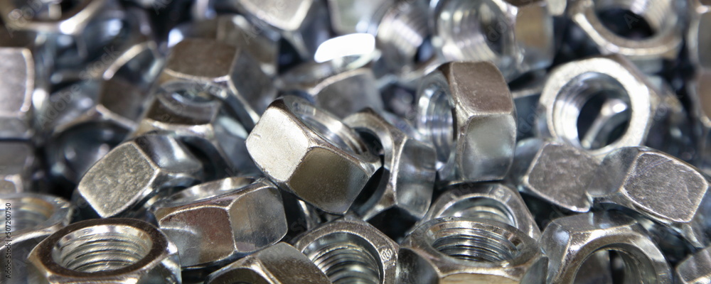 A lot of new gray nuts close up. Galvanized construction fasteners. Technical wide texture for background.