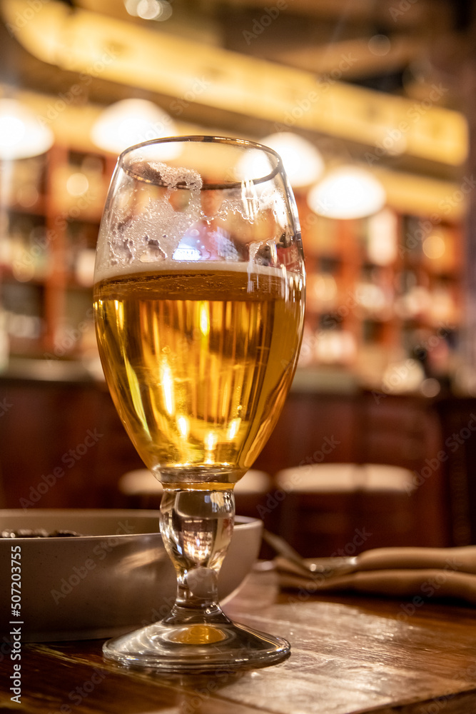 Glass of beer, blurred bokeh bar background.