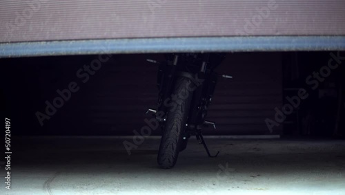 Reveal shot of a black motorcycle from yamaha standing with lights on inside a garage with a automatic garage door which is openend to reveal the motorbike photo