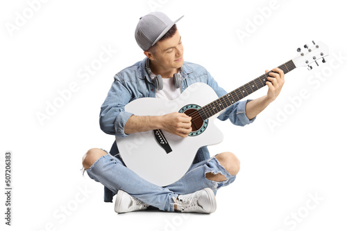 Young male guitarist sitting on the floor playing an acoustic guitar
