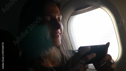 Close-up of a young relaxed woman using a smartphone app at the airplane window.