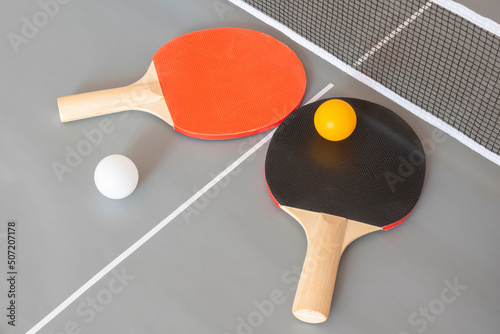 Two ping pong table tennis rackets and balls on a gray table