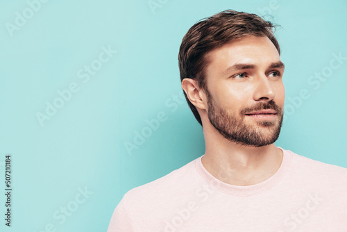 Closeup portrait of handsome smiling stylish hipster lambersexual model. Sexy man dressed in pink T-shirt and trousers. Fashion male isolated on blue wall in studio