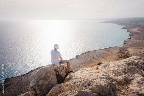 Summer landscape in Cyprus. View from the top of Cape Greco. Morning sunrise in Cyprus. A man sitting on the edge of a cliff and admires the scenery