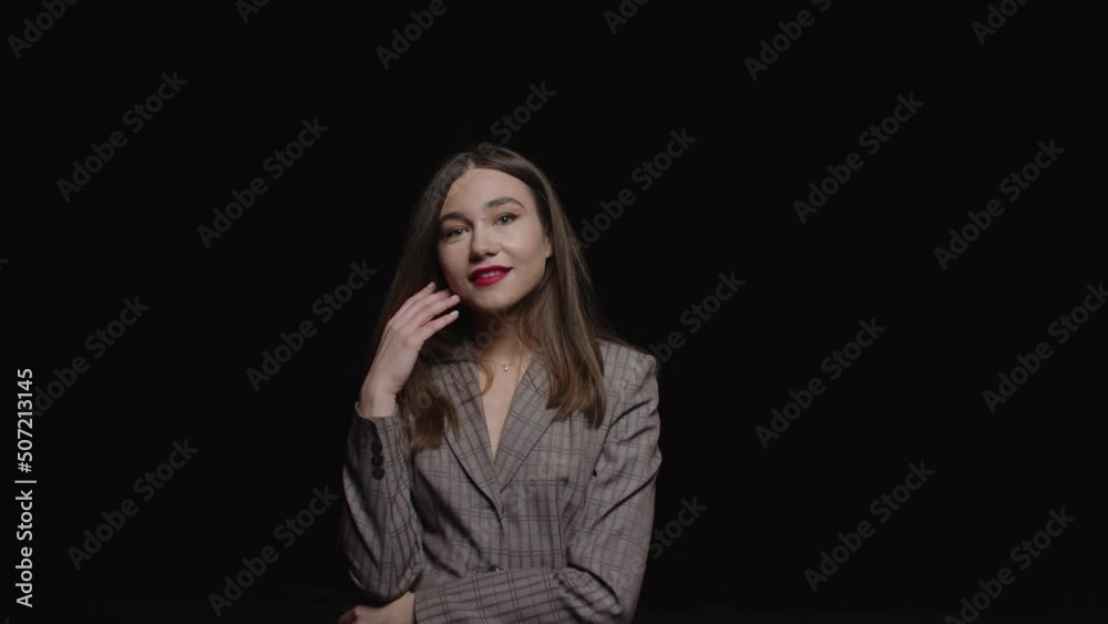 A stylish young brunette in a jacket feels happy and poses for the camera on a black background. A stylish young brunette in a jacket feels happy and poses for the camera on a black background.