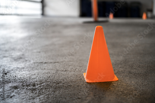Safety cone on driveway in parking garage while repair work is in progress or cleaning. Close up. Parkade with elastomeric traffic deck coating and closed parking gate background. Selective focus. photo