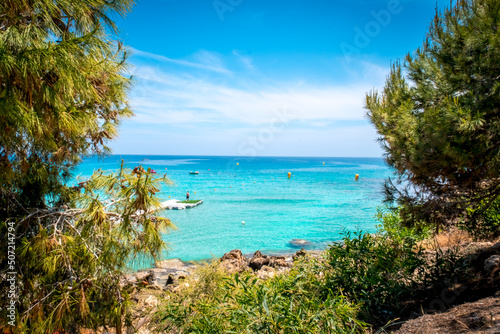 Summer landscape on Konnos beach in Cyprus. View of the turquoise sea through the branches of trees