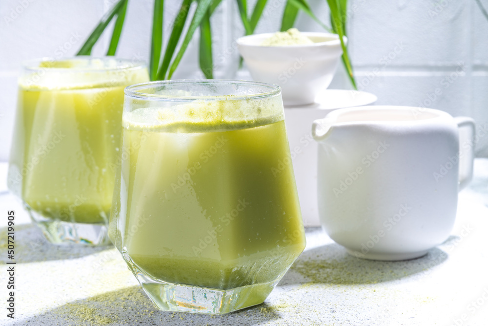 Cold matcha green tea drink. Iced matcha latte cocktail in two glasses with summer tropical palm leaves on white background copy space Cold matcha green tea drink. Iced matcha latte cocktail in two glasses with summer tropical palm leaves on white background copy space
