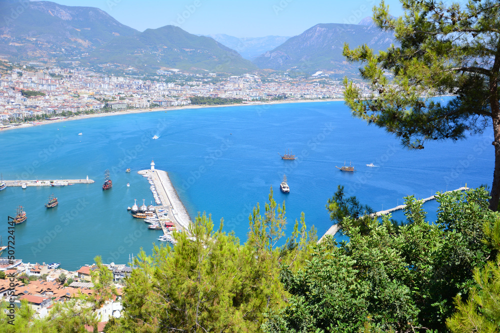 Alanya seaport with lighthouse and waterfront, view from top of mountain through pine trees