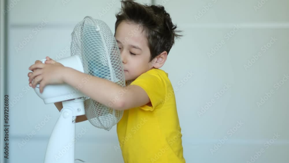 preschool boy cooling in front of fan. Little child refreshing from heat in front of small fan at home. Cute small kid play with ventilator blowing cool wind alone. preschool boy cooling in front of fan. Little child refreshing from heat in front of small fan at home. Cute small kid play with ventilator blowing cool wind alone.