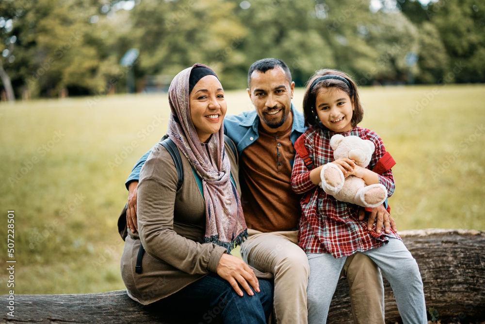 Portrait of happy Muslim parents with daughter in park looking at camera.