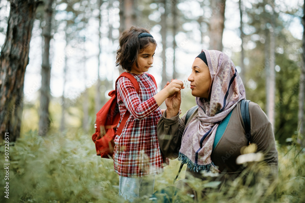 Fototapeta premium Small Muslim girl and her mother smelling flowers while spending day in the woods.