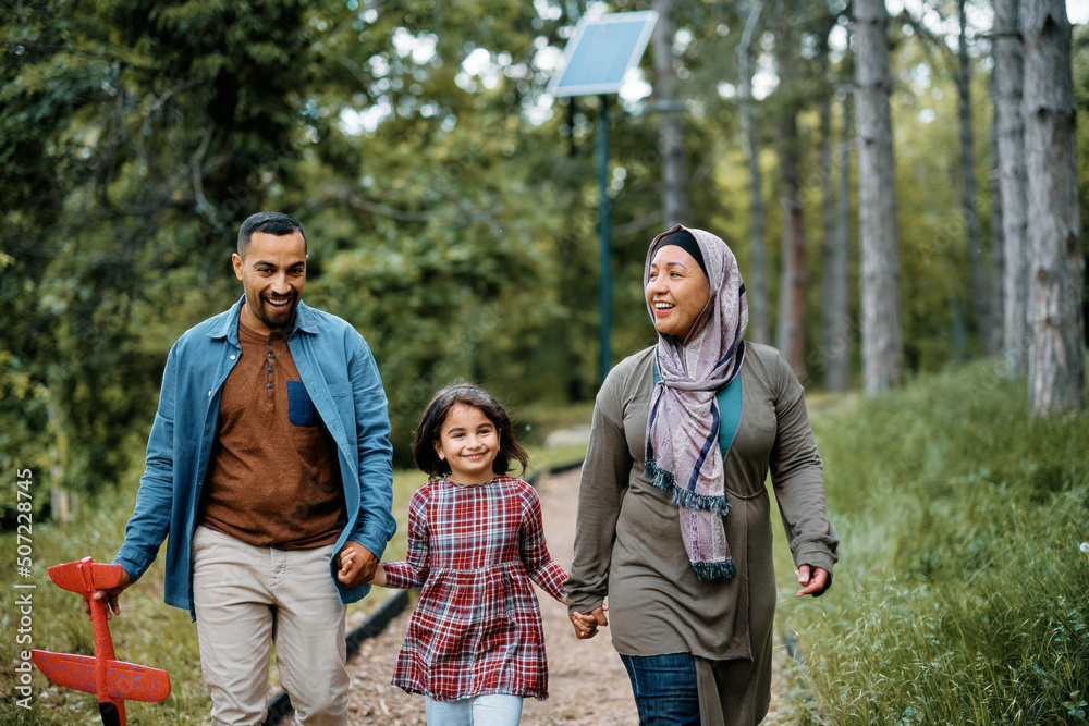 Happy Middle Eastern family holding hands while walking through park. Happy Middle Eastern family holding hands while walking through park.