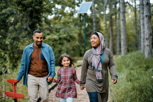 Happy Middle Eastern family holding hands while walking through park.