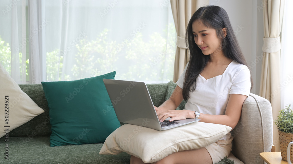 Beautiful asian woman in casual clothes resting on couch and using computer laptop Beautiful asian woman in casual clothes resting on couch and using computer laptop