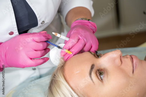 Close up hands of cosmetologist makes anti-aging injection by syringe in forehead against wrinkle in medical office. Concept of beauty, self and skin care. Selective focus