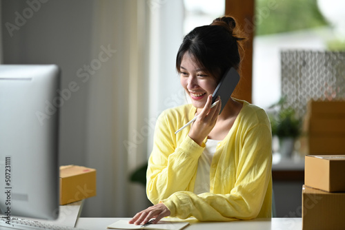 Wallpaper Mural Smiling female small business owner using computer and talking on mobile phone for confirming orders from customer. Online selling, e-commerce concept Torontodigital.ca