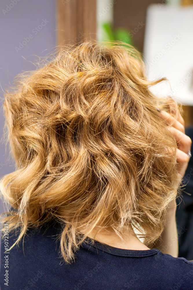 Rear view of young woman checking her new curly brown hairstyle at the hairdresser salon Rear view of young woman checking her new curly brown hairstyle at the hairdresser salon