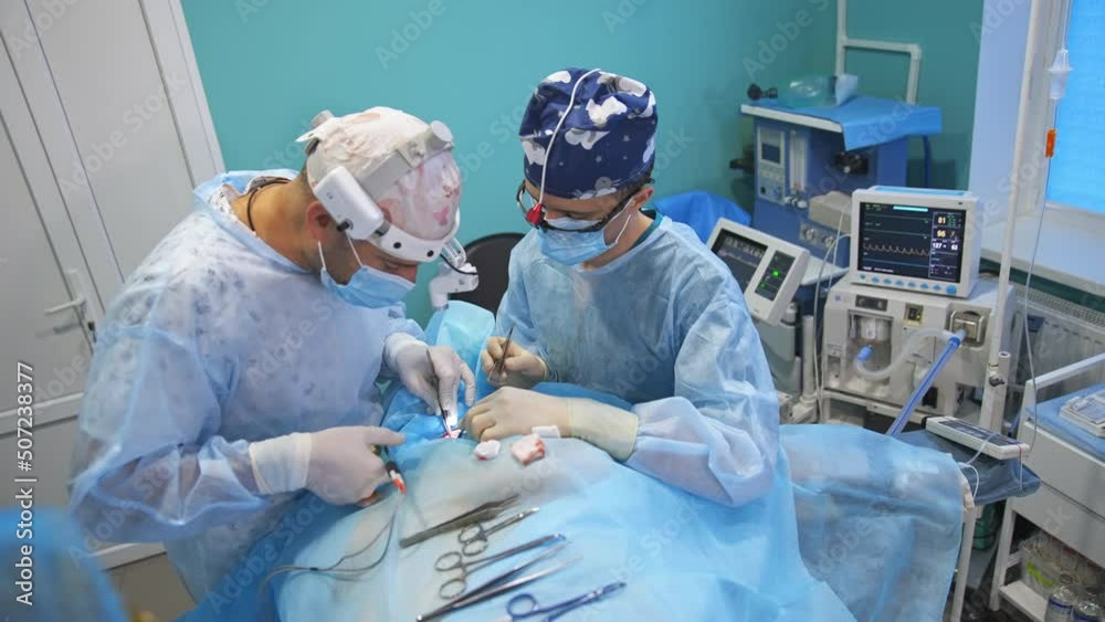 Doctors in device glasses using metal tools placed on the patient. Medical equipment behind the doctors at backdrop. Doctors in device glasses using metal tools placed on the patient. Medical equipment behind the doctors at backdrop.