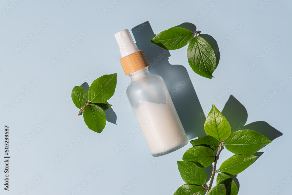 Transparent glass cosmetic bottle with a pusher on a blue background with tropical leaves. Natural cosmetics concept, natural essential oil and skin care products - obrazy, fototapety, plakaty 
