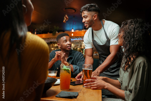 Diverse group of friends out for dinner being served by waiter  photo