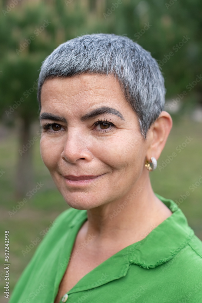 Portrait of pretty woman with grey hair in park. Female model with short grey hair in bright clothes looking at camera. Beauty, portrait concept Portrait of pretty woman with grey hair in park. Female model with short grey hair in bright clothes looking at camera. Beauty, portrait concept