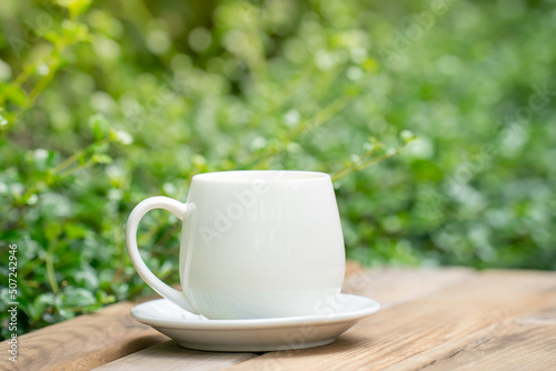 white ceramic coffee mug On the wooden floor, green tree bokeh background. soft focus.shallow focus effect.