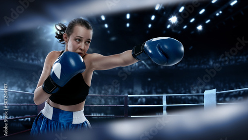 Collage with young female professional boxer in boxing gloves punching in flashlights over dark drawn boxing ring background. Concept of sport, studying, competition