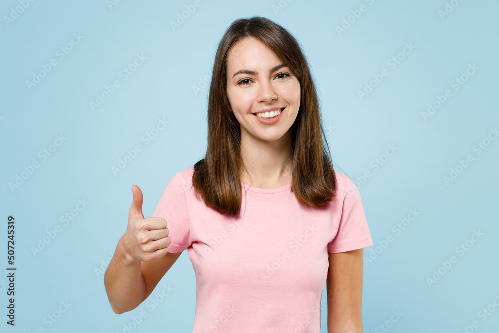 Young smiling satisfied fun cool happy woman 20s wear pink t-shirt look camera showing thumb up like gesture isolated on pastel plain light blue background studio portrait. People lifestyle concept Young smiling satisfied fun cool happy woman 20s wear pink t-shirt look camera showing thumb up like gesture isolated on pastel plain light blue background studio portrait. People lifestyle concept