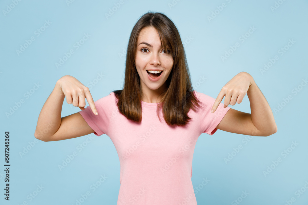 Young amazed happy woman 20s wear pink t-shirt point index finger down on workspace area mock up copy space isolated on pastel plain light blue background studio portrait. People lifestyle concept