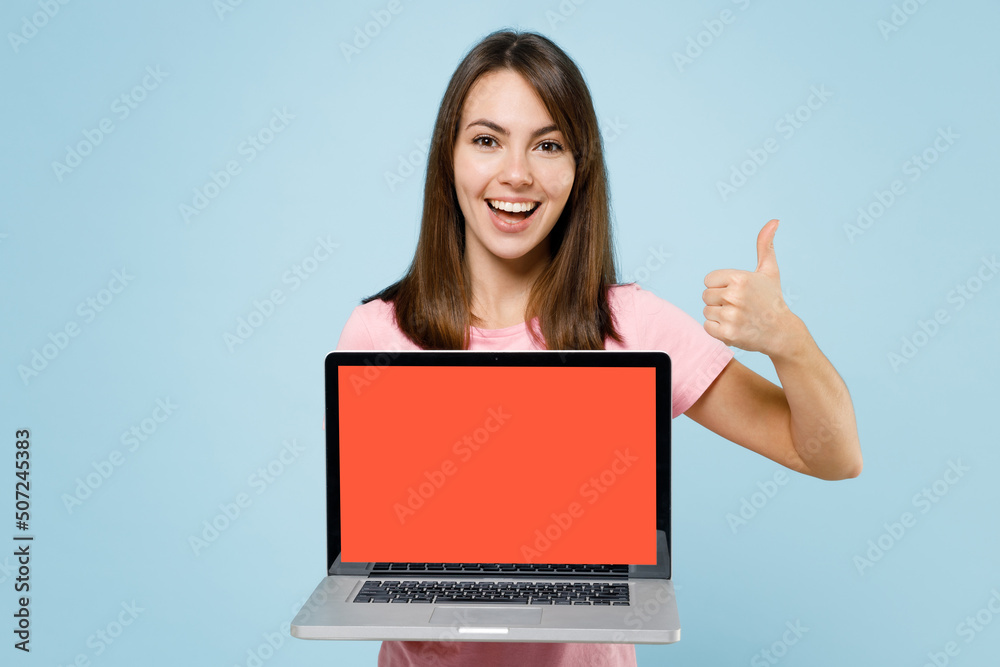 Young smiling fun caucasian woman 20s in pink t-shirt hold use work on laptop pc computer with blank screen workspace area show thumb up isolated on pastel plain light blue background studio portrait Young smiling fun caucasian woman 20s in pink t-shirt hold use work on laptop pc computer with blank screen workspace area show thumb up isolated on pastel plain light blue background studio portrait