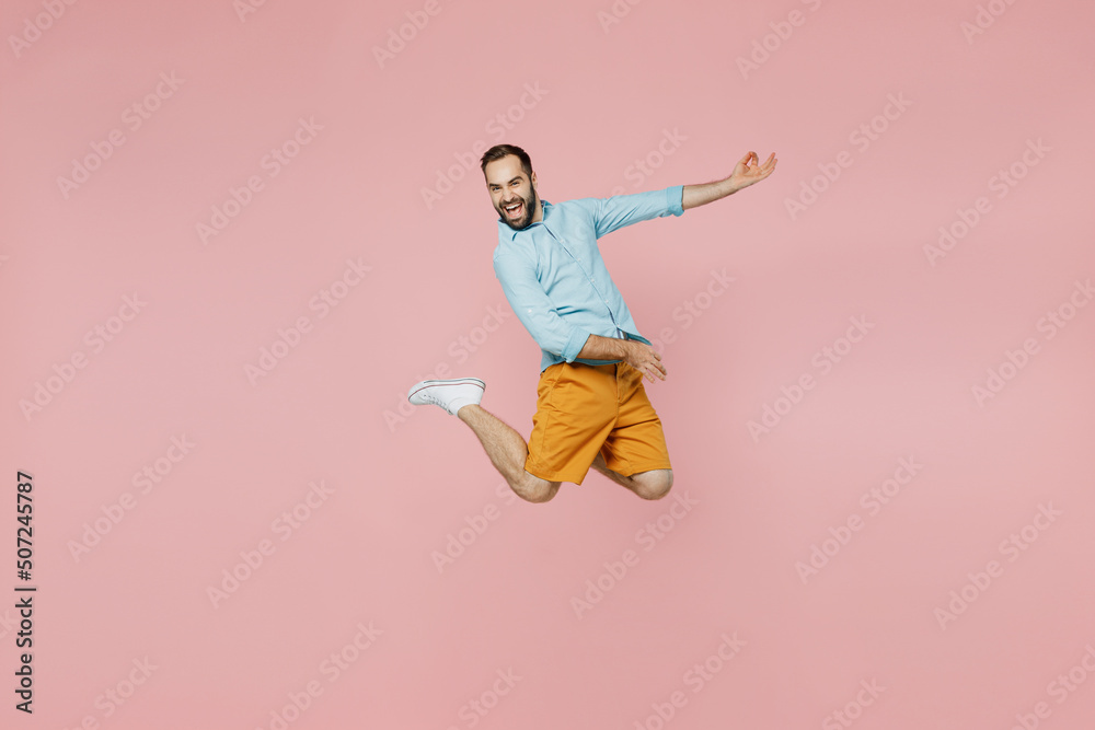 Full body young expressive singer musician man 20s wear classic blue shirt do playing guitar gesture jump high isolated on plain pastel light pink background studio portrait. People lifestyle concept. Full body young expressive singer musician man 20s wear classic blue shirt do playing guitar gesture jump high isolated on plain pastel light pink background studio portrait. People lifestyle concept.