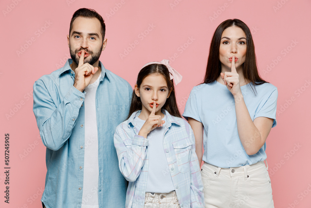 Young parents mom dad with child kid daughter teen girl in blue clothes say hush be quiet with finger on lips shhh gesture isolated on plain pastel light pink background Family day parenthood concept Young parents mom dad with child kid daughter teen girl in blue clothes say hush be quiet with finger on lips shhh gesture isolated on plain pastel light pink background Family day parenthood concept