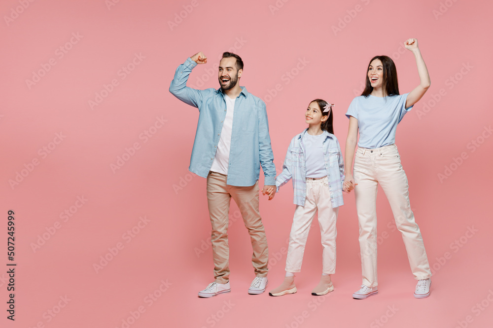 Full size young parents mom dad with child kid daughter teen girl in blue clothes do winner gesture celebrate clenching fists say yes isolated on plain pastel light pink background Family day concept