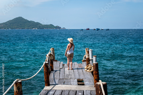 Mujer mirando el horizonte en muelle, frente a mar azul