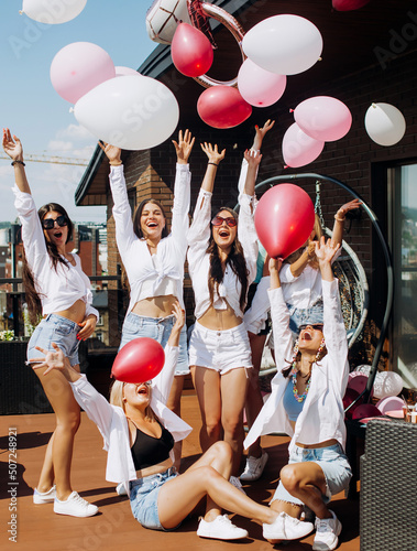 Happy girls dancing and having fun on the roof at home. Girlfriends throw helium balls up. Maiden evening.