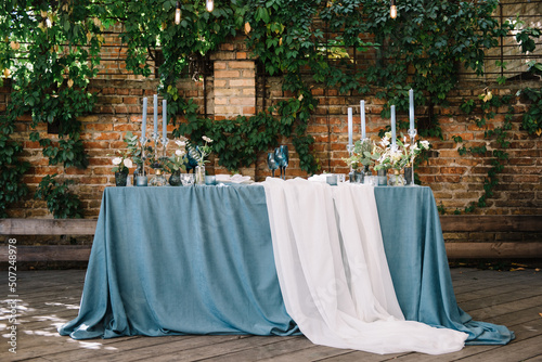 Stylish wedding table decoration and table setting. Blue tablecloth. Outdoor wedding party. Vintage light bulb on a brick walls