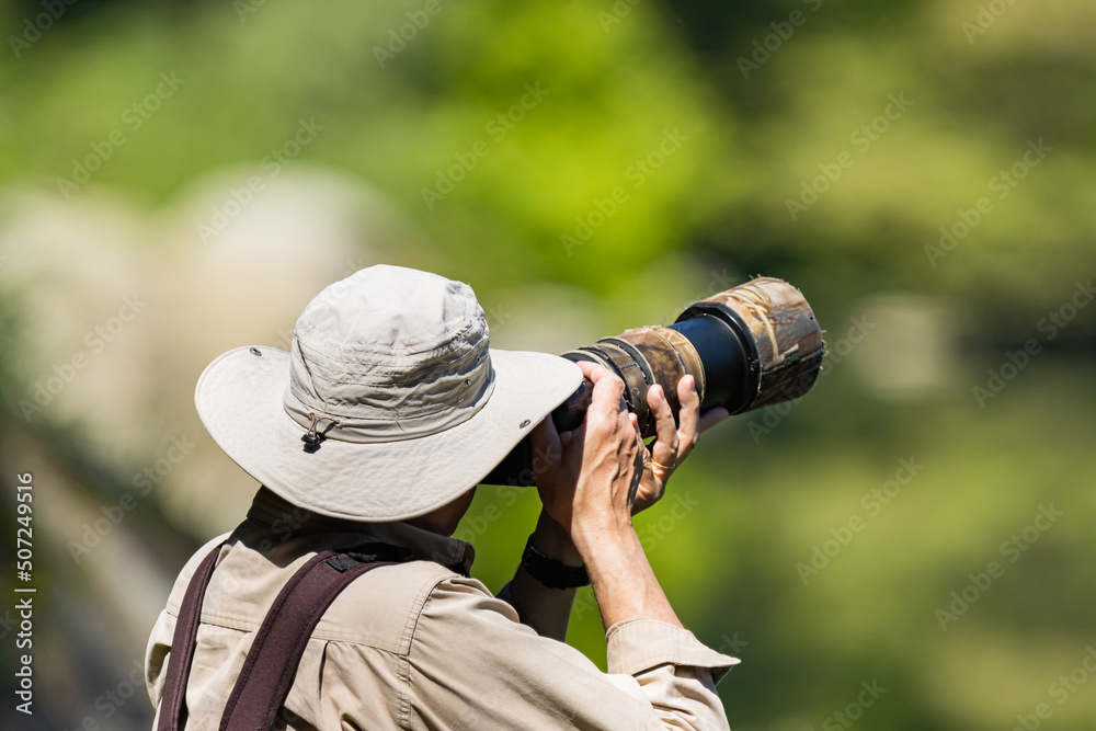 Wildlife photographer using a telephoto lens with camouflage coating, selective focus on the cap. Wildlife photographer using a telephoto lens with camouflage coating, selective focus on the cap.