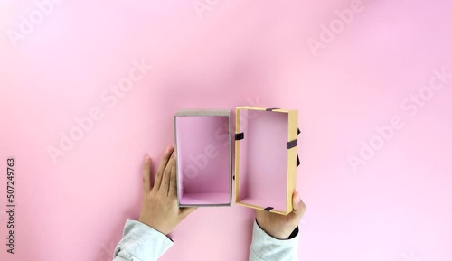 Top view - Female hand holding and opening a beautiful blank golden gift box with a gray bow on a light gray background with copy space on right. photo