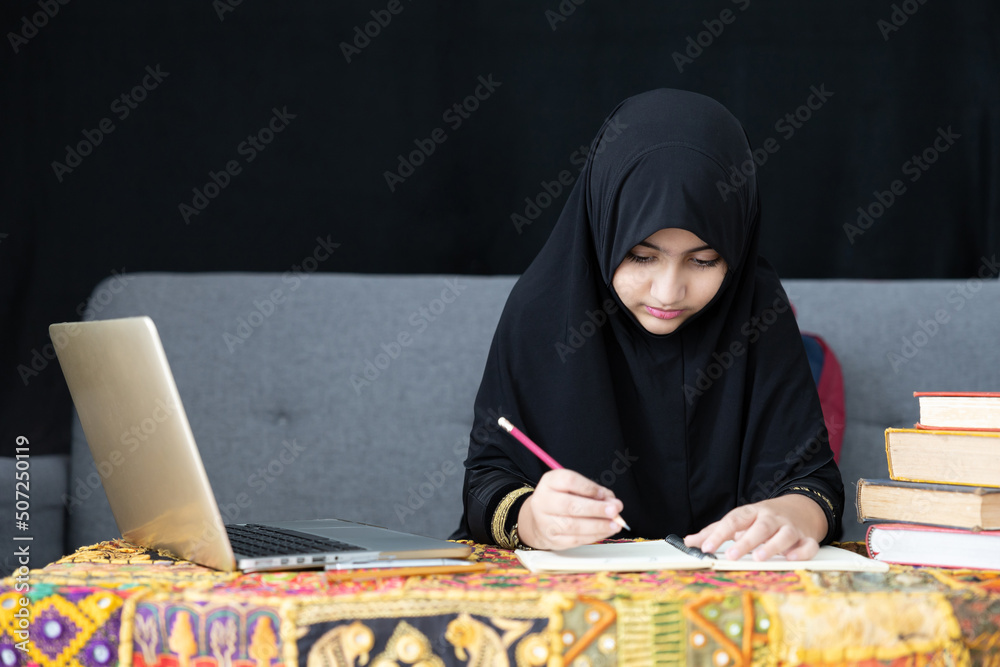 muslim girl writing on notebook, using a laptop computer and online learning at home muslim girl writing on notebook, using a laptop computer and online learning at home