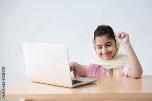 muslim girl in hijab using a laptop computer and online learning or working on the table © offsuperphoto