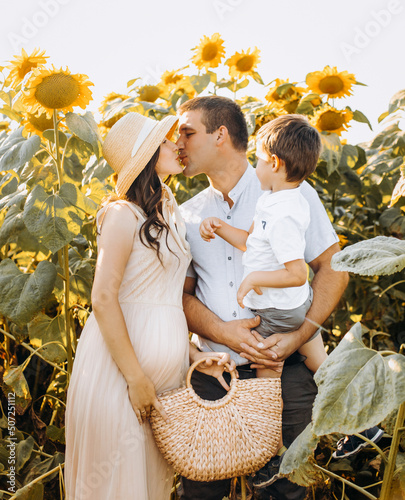 Portrait of a young beautiful family in a field with yellow blooming sunflowers. Man, woman and child, boy. Camping at sunset in summer. Have fun, hugs.