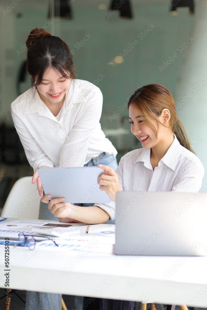 Businesswoman colleagues in the office discussing work and planning projects together on a tablet at their desk. Businesswoman colleagues in the office discussing work and planning projects together on a tablet at their desk.