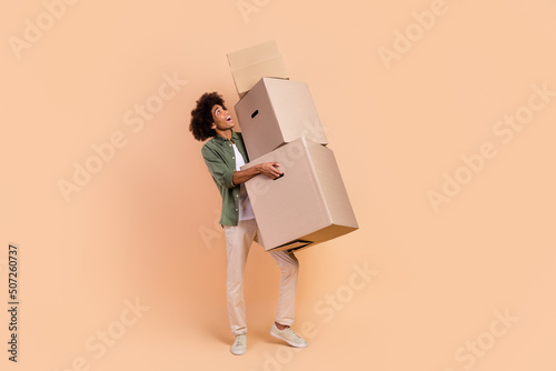 Full length body size view of attractive cheerful wavy-haired guy carrying office boxes isolated over beige pastel color background photo