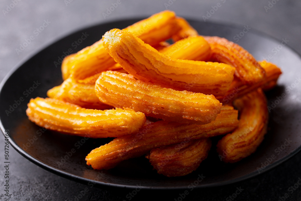 Churros dessert on black plate. Grey background. Close up. Churros dessert on black plate. Grey background. Close up.