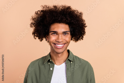 Portrait of attractive funky cheerful wavy-haired guy with chevelure wearing green shirt isolated over beige pastel color background